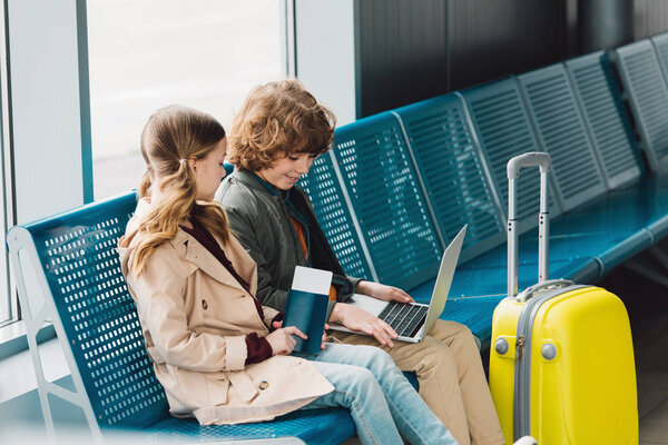 children sitting on blue seats near yellow suitcase in waiting hall in airport 
