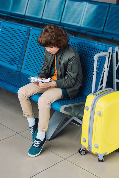 preteen boy holding toy plane while sitting in airport departure lounge