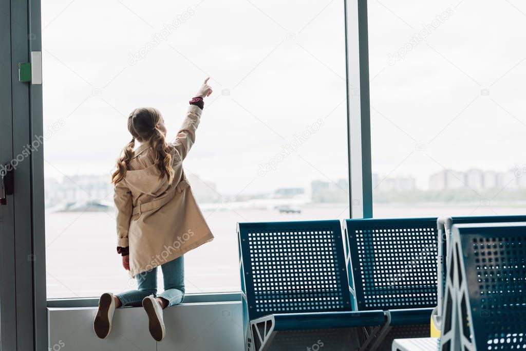 back view of preteen kid pointing with finger at window in airport