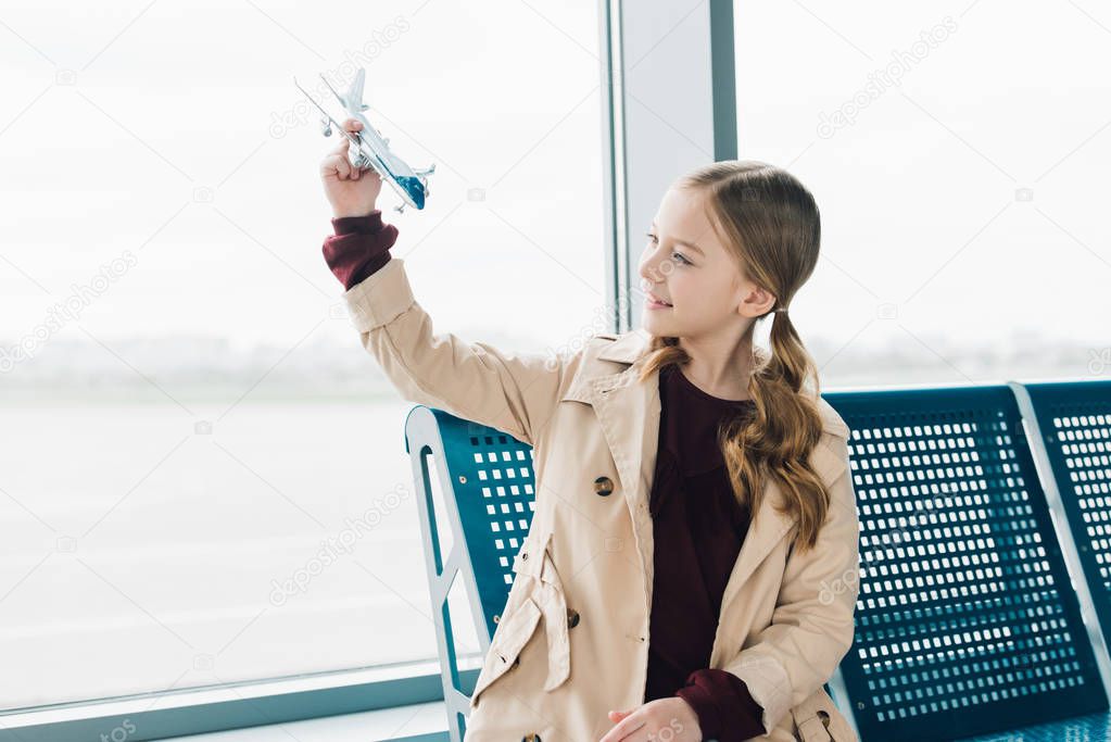 smiling preteen kid holding toy plane in airport departure lounge