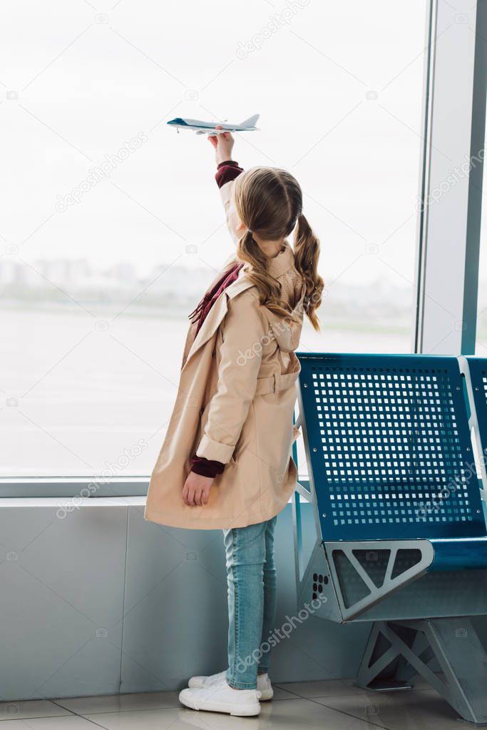 Back view of preteen kid holding toy plane in airport departure lounge