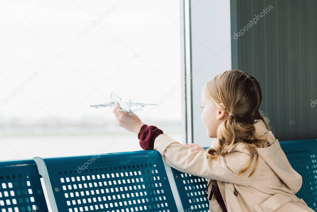 preteen kid holding toy plane in airport departure lounge