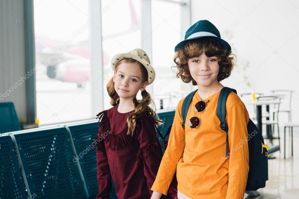 adorable preteen children in hats looking at camera in waiting hall