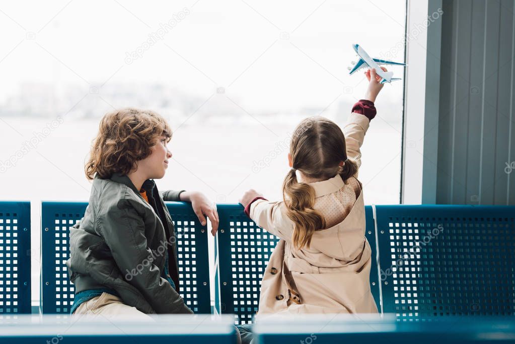 cute preteen kids sitting in waiting hall and playing with toy plane