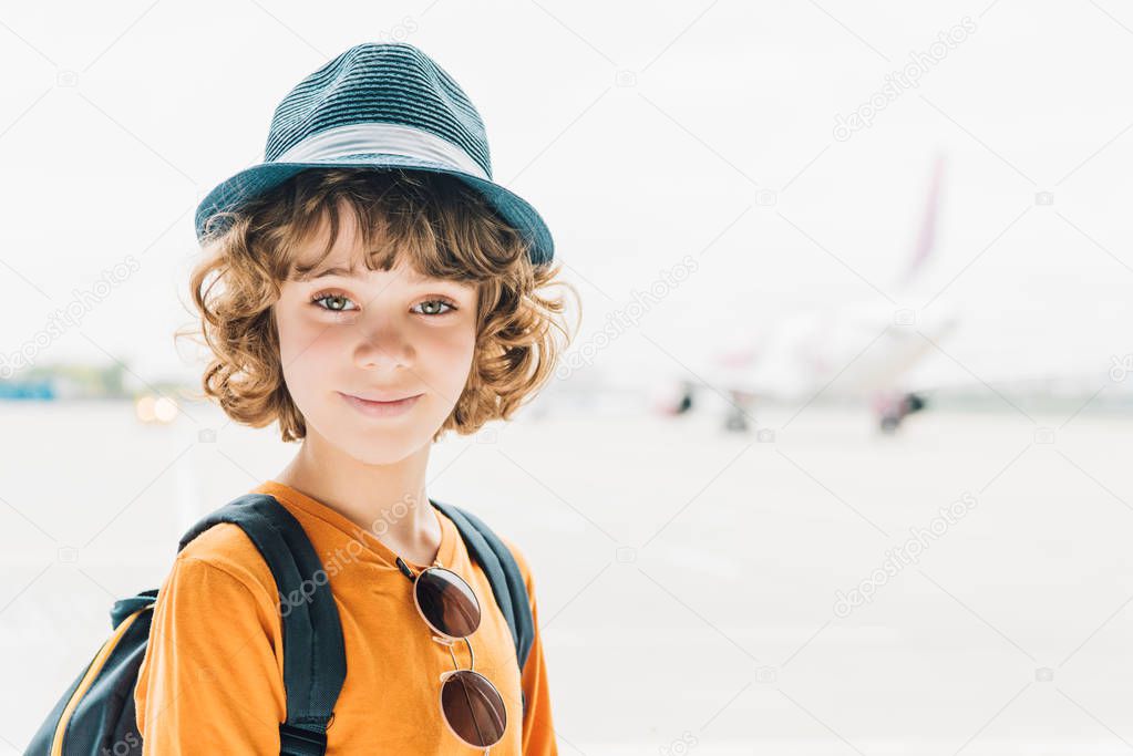 adorable preteen kid in hat looking at camera in airport with copy space