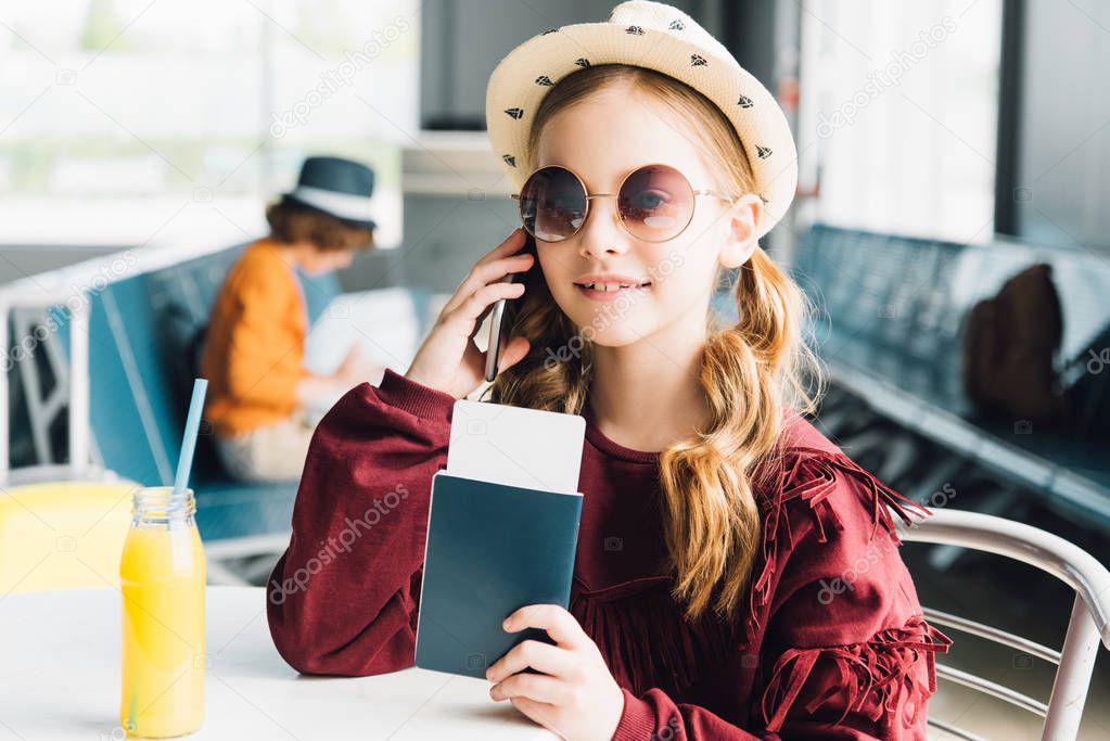 smiling preteen kid holding passport and talking on smartphone in waiting hall