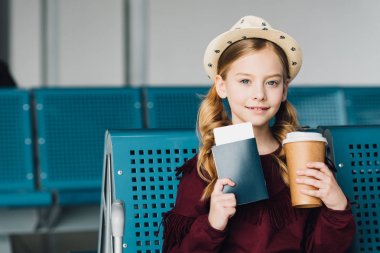 smiling preteen kid with passport, coffee to go and air ticket in airport clipart