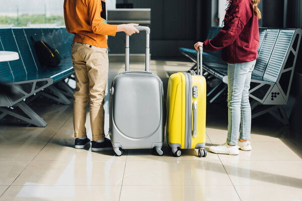 Задний вид на подростков с чемоданами в зале ожидания
