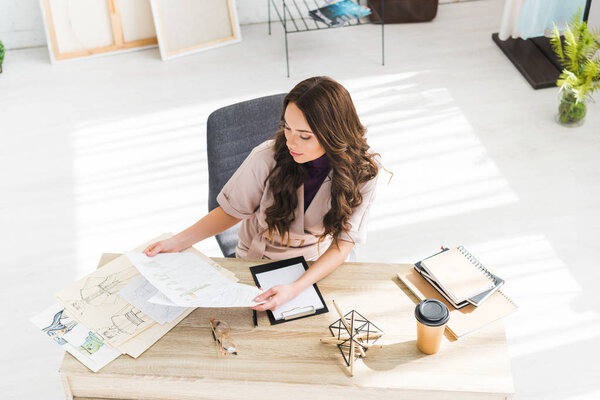 вид кудрявого дизайнера, смотрящего на эскизы мод в дизайнерской студии
 