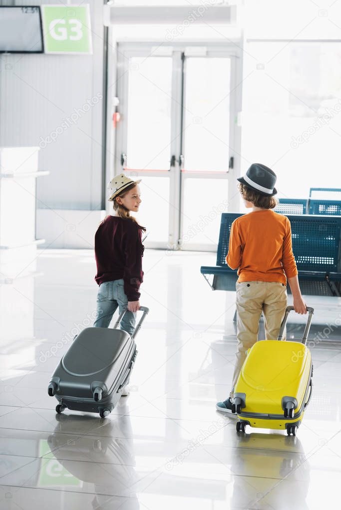 Cropped view of preteen kids with suitcases in waiting hall in airport