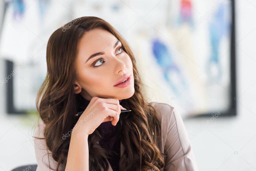 dreamy curly young woman thinking and holding pen