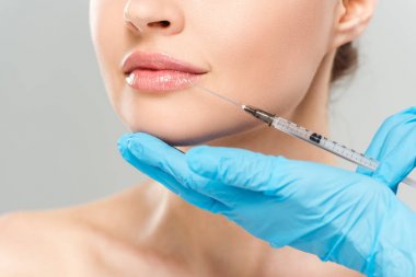 cropped view of cosmetologist in blue latex gloves holding syringe near face of woman isolated on grey  clipart