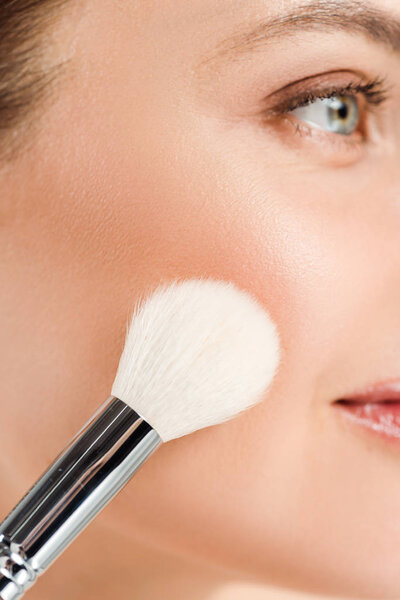 cropped view woman applying blush on cheek with cosmetic brush 