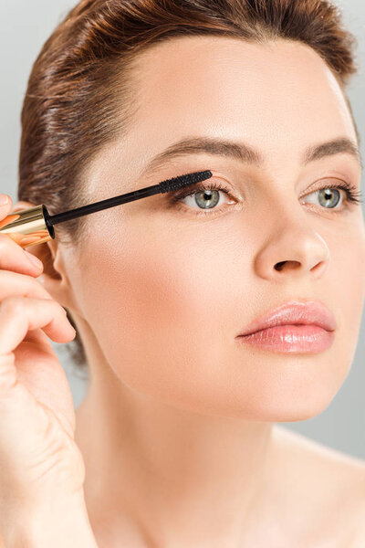 attractive woman applying mascara isolated on grey 