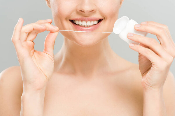 cropped view of cheerful naked woman holding dental floss near teeth isolated on grey 