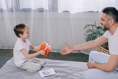 gülümseyen baba yakınında otururken babalar gün hediye kutusu tutan sevimli çocuk 