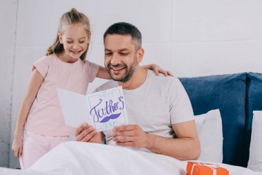 cheerful daughter embracing happy dad holding fathers day greeting card