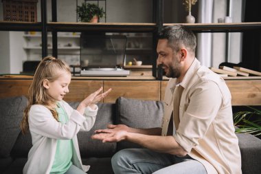 cheerful dad with adorable daughter having fun while sitting on sofa at home 