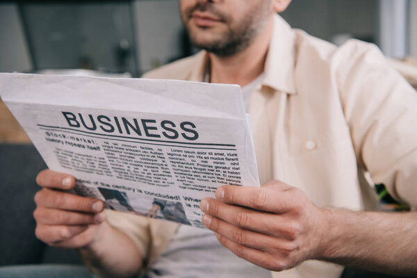 cropped shot of bearded man reading business newspaper at home