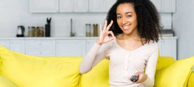 happy african american woman with remote controller in hand showing ok sign clipart