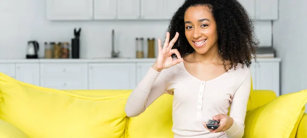 Ok記号を示す手にリモコンを持つ幸せなアフリカ系アメリカ人女性 — ストック写真