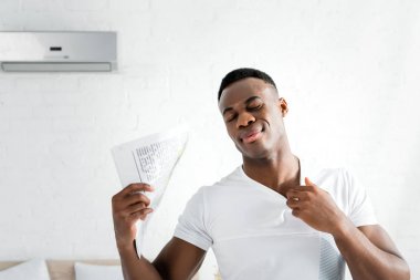 terli afro-amerikan adam gözleri kapatarak, ısı sıcaklığı ile beyaz odada duran, elinde gazete tutarak