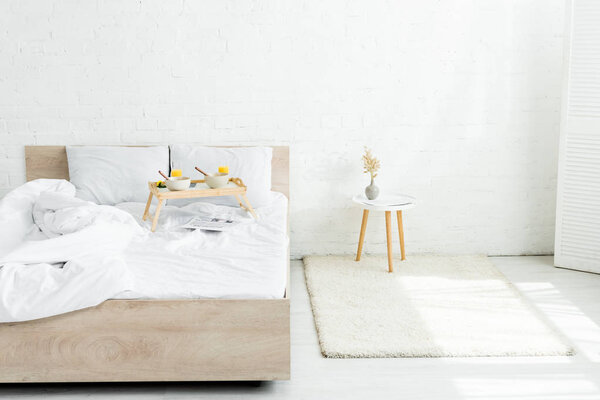 tray table with breakfast on bed in white, bright room