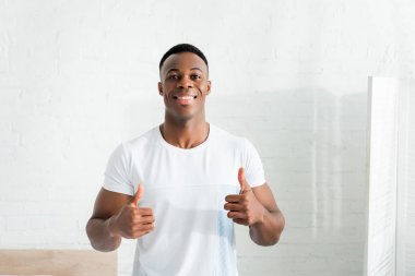 front view of happy african american man showing thumbs up, looking at camera clipart