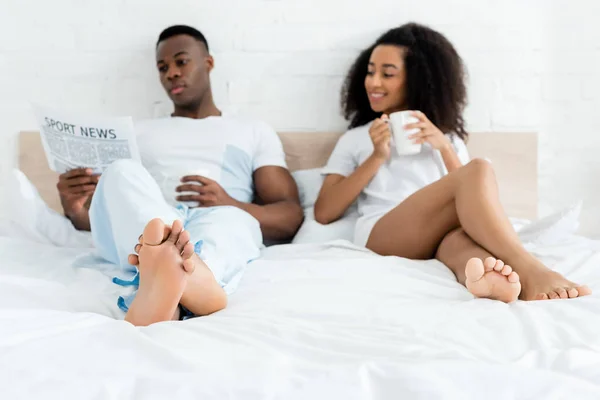 African American Woman Lying Bed Man Cup Newspaper — Stock Photo, Image