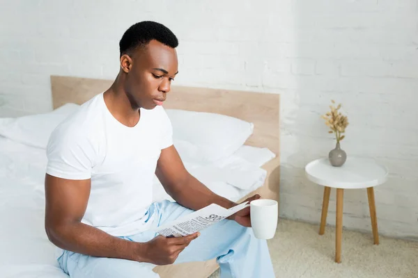 Hombre Afroamericano Tranquilo Sentado Cama Leyendo Periódico Sosteniendo Taza Con — Foto de Stock