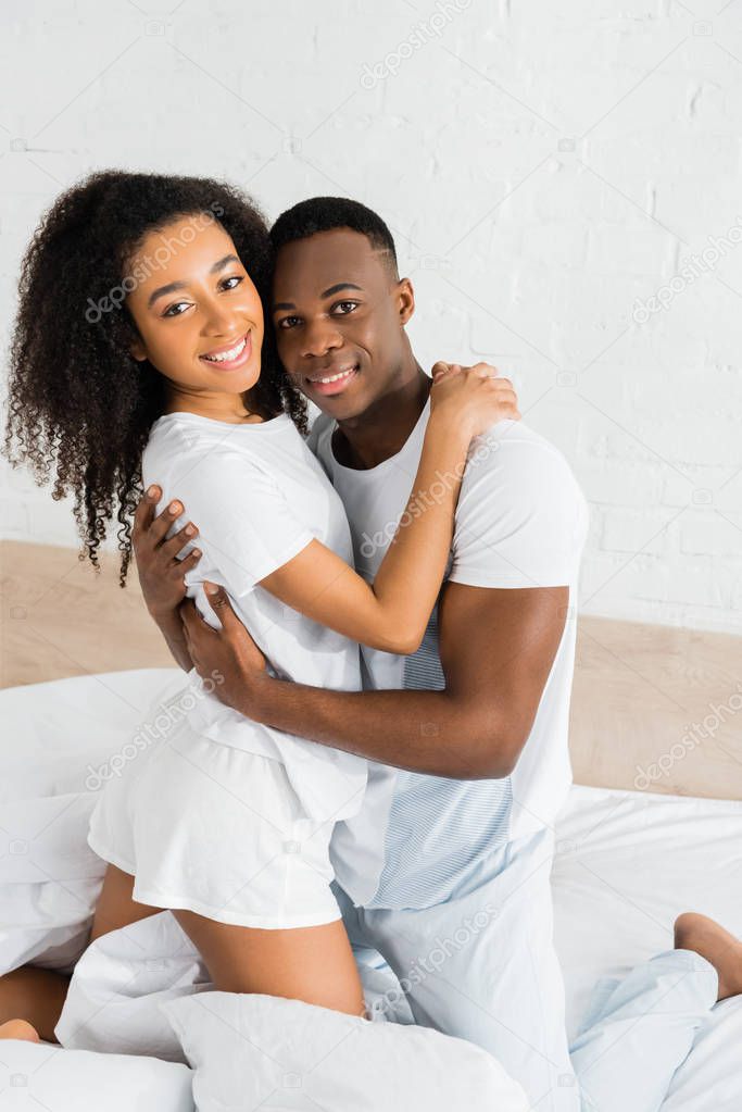 african american cuople standing on bed, hugging each other and looking at camera