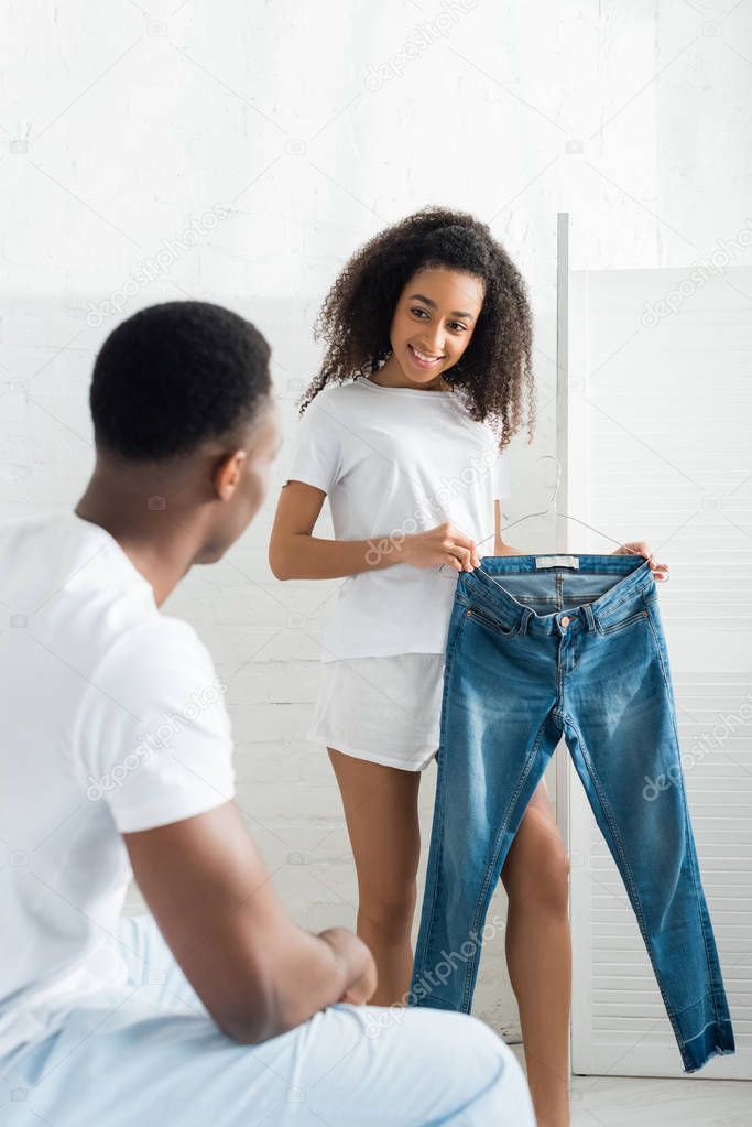selective focus of happy african american woman showing denim jeand pants to boyfriend