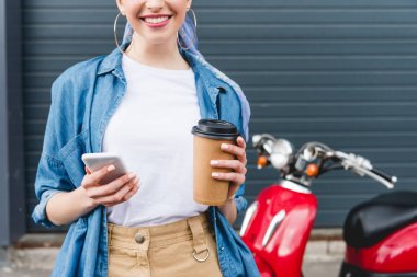 kırmızı scooter yanında duran güzel kız kırpılmış görünümü, kahve ve akıllı telefon ile kağıt fincan tutarak