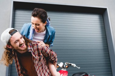 Genç adam ve kız gülüyor, kırmızı scooter 'ın yanında dikilirken sırtına biniyor. 