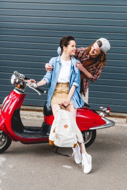 beautiful girl sitting on red scooter and young man looking at her  clipart