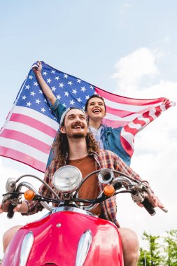 low angle view of beautiful girl standing behind young man and holding flag on sky background clipart