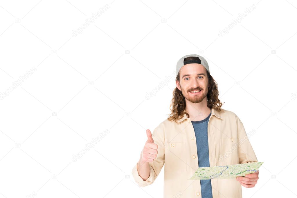 front view of young man smilling at camera, holding map and showing thumb up isolated on white