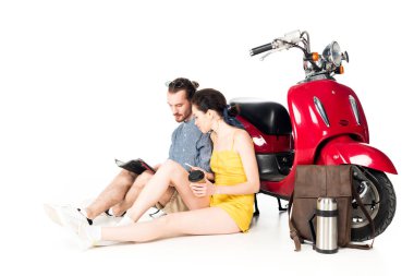 Genç adam ve kız kırmızı scooter 'ın yanında oturuyor ve beyaz haritaya bakıyorlar.