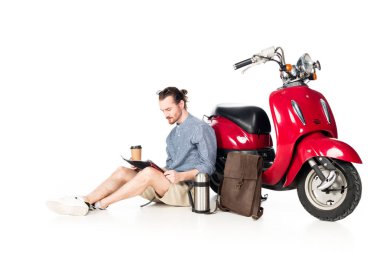  kağıt bardak tutan genç adam, harita bakarak ve beyaz izole kırmızı scooter yakınında oturan