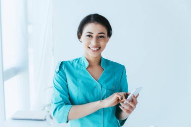 akıllı telefon kullanarak neşeli latin hemşire ve kamera gülümseyen