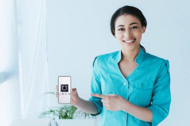 Kiev, Ukrayna - 26 Nisan 2019: Ekranda Uber uygulaması ile akıllı telefon gösteren neşeli latin doktor.