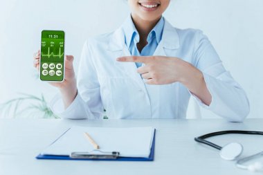 ekranda kalp atışı oranı ile akıllı telefonda parmak ile işaret gülümseyen latin doktor kırpılmış atış