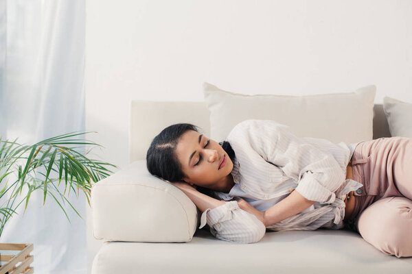 beautiful tired latin woman lying with closed eyes on sofa at home