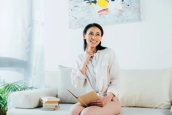 Vrolijke Latijnse Vrouw Die Boek Houdt Wegkijkt Terwijl Thuis Bank — Stockfoto