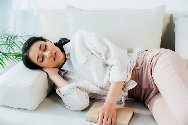 beautiful young woman sleeping with book while lying on couch at home