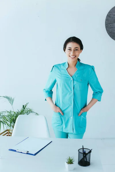 Attractive Latin Doctor Smiling Camera While Standing Workplace Hands Pockets — Stock Photo, Image