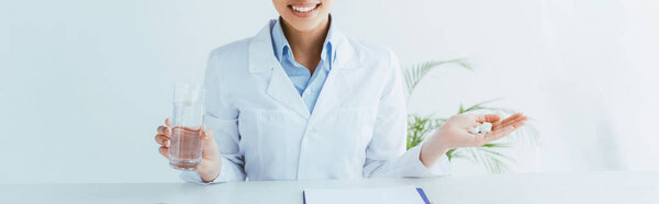 panoramic shot of smiling doctor with handful of pills and glass of water