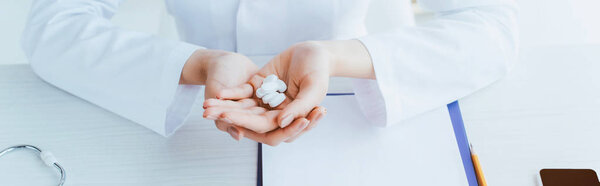 panoramic shot of doctor holding pills while sitting at workplace