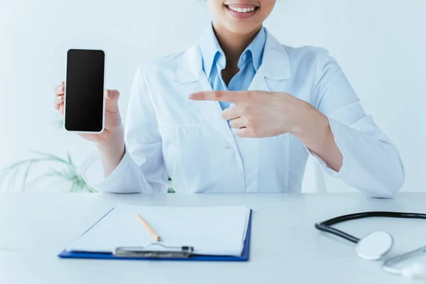 Częściowy Widok Uśmiechnięty Łaciński Lekarz Wskazując Palcem Smartfonie Pustym Ekranem — Zdjęcie stockowe