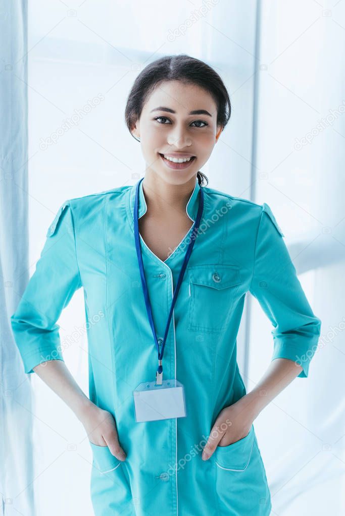beautiful latin doctor holding hands in pockets and smiling at camera